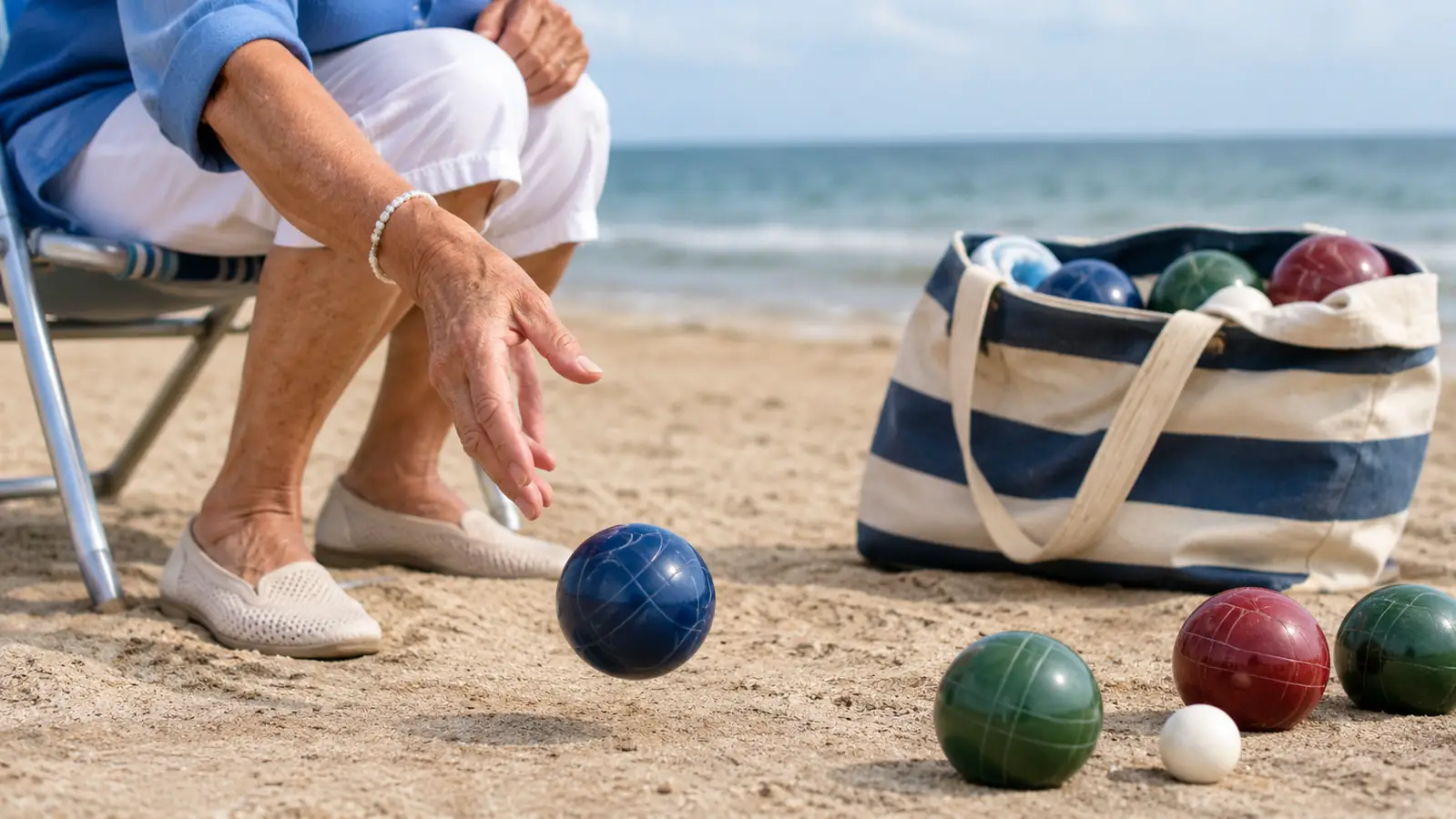 A hand rolling a bocce ball across packed sand near the water.