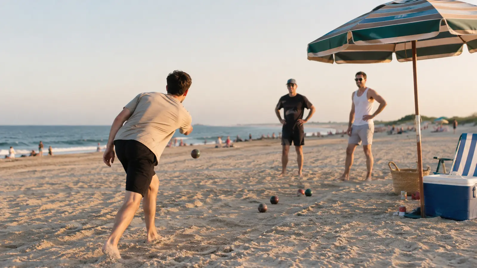 A cooler, two umbrellas and a wagon at the edge of the sand, with a bocce game in front