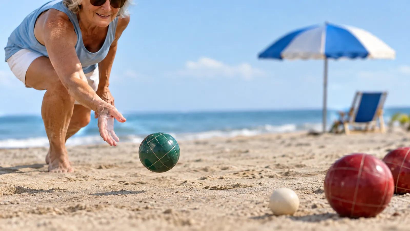 An older woman tossing a bocce ball underhand toward a small target ball on packed beach sand