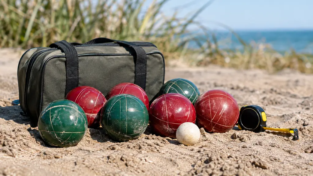 Bocce balls resting on the sand beside a zippered carrying case and a measuring tape