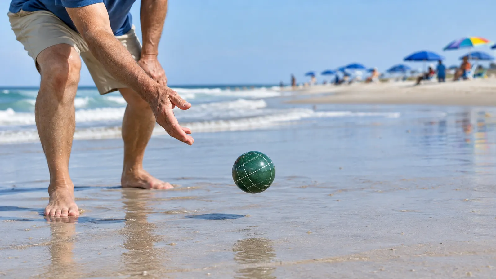 A hand releasing a bocce ball in a low underhand toss on firm, wet sand near the water