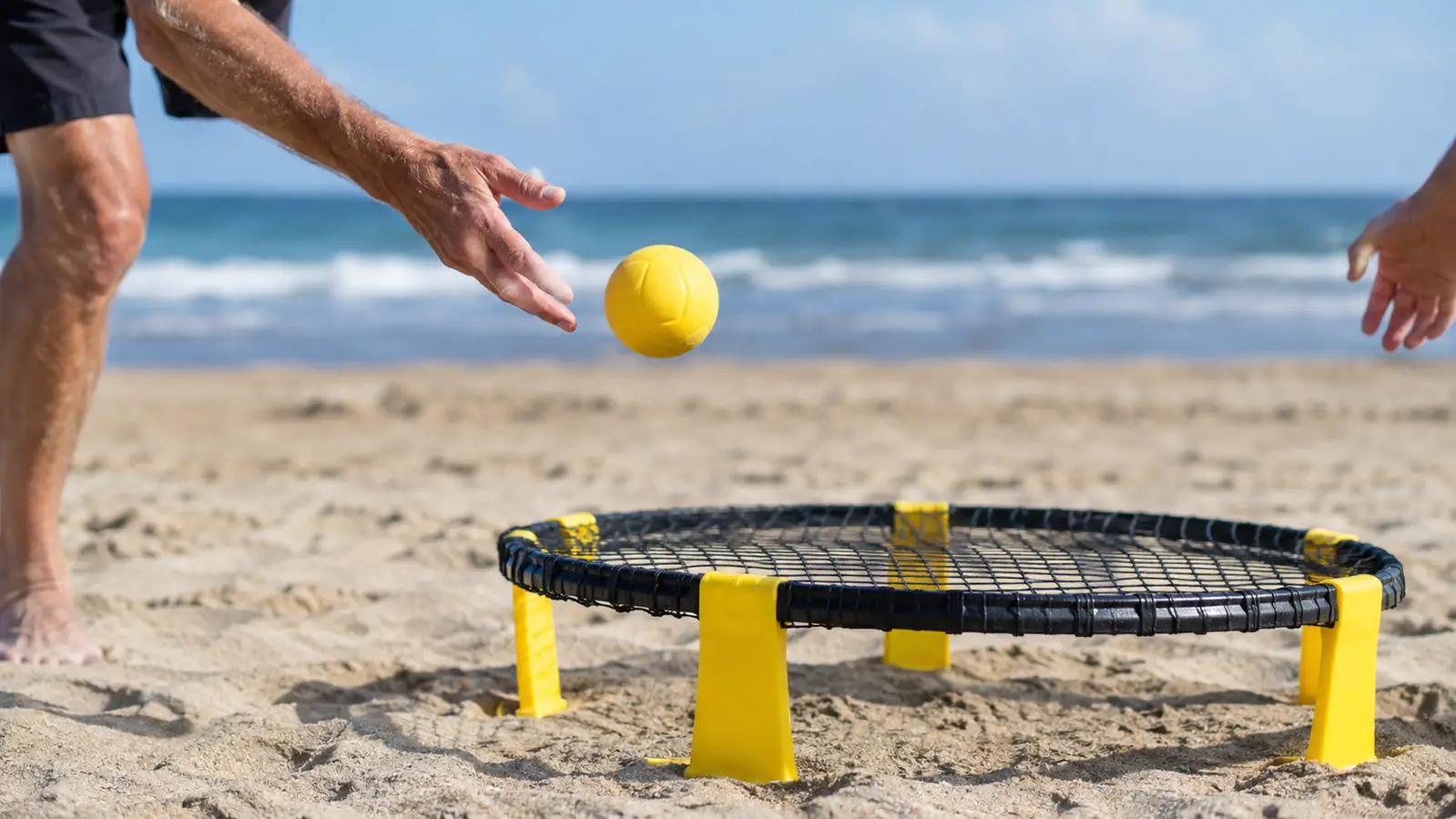 A hand serving a ball into a roundnet net set up on beach sand