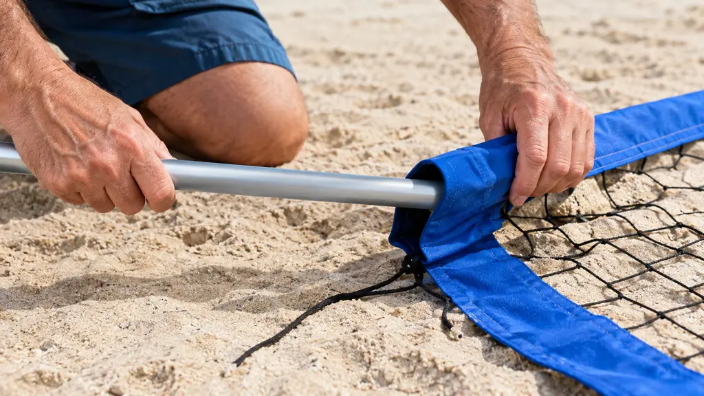 Hands sliding a pole through the sleeve of a volleyball net laid out on the sand